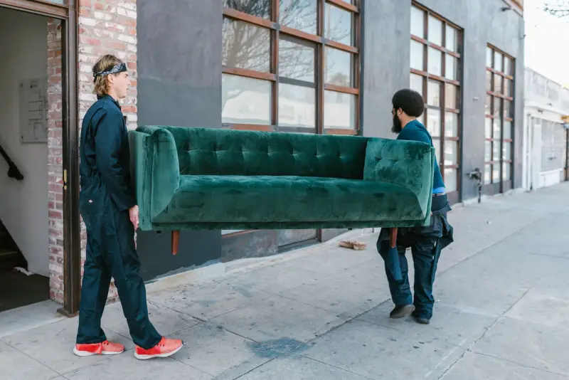 Two movers carrying a sofa along a city sidewalk