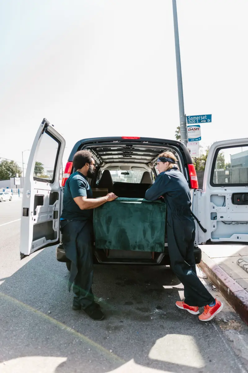 Two movers loading a sofa into the back of a van