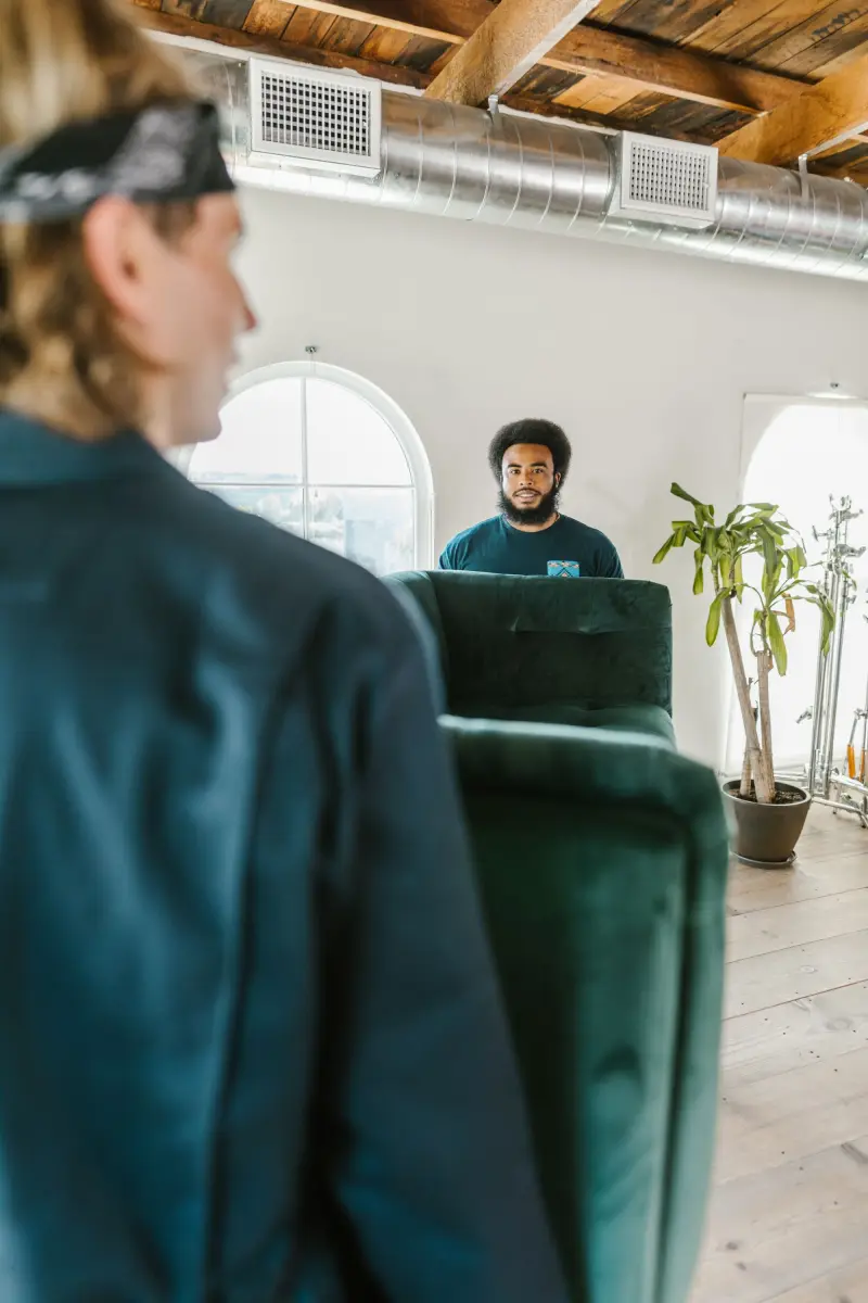 Two movers carrying a green couch through an apartment