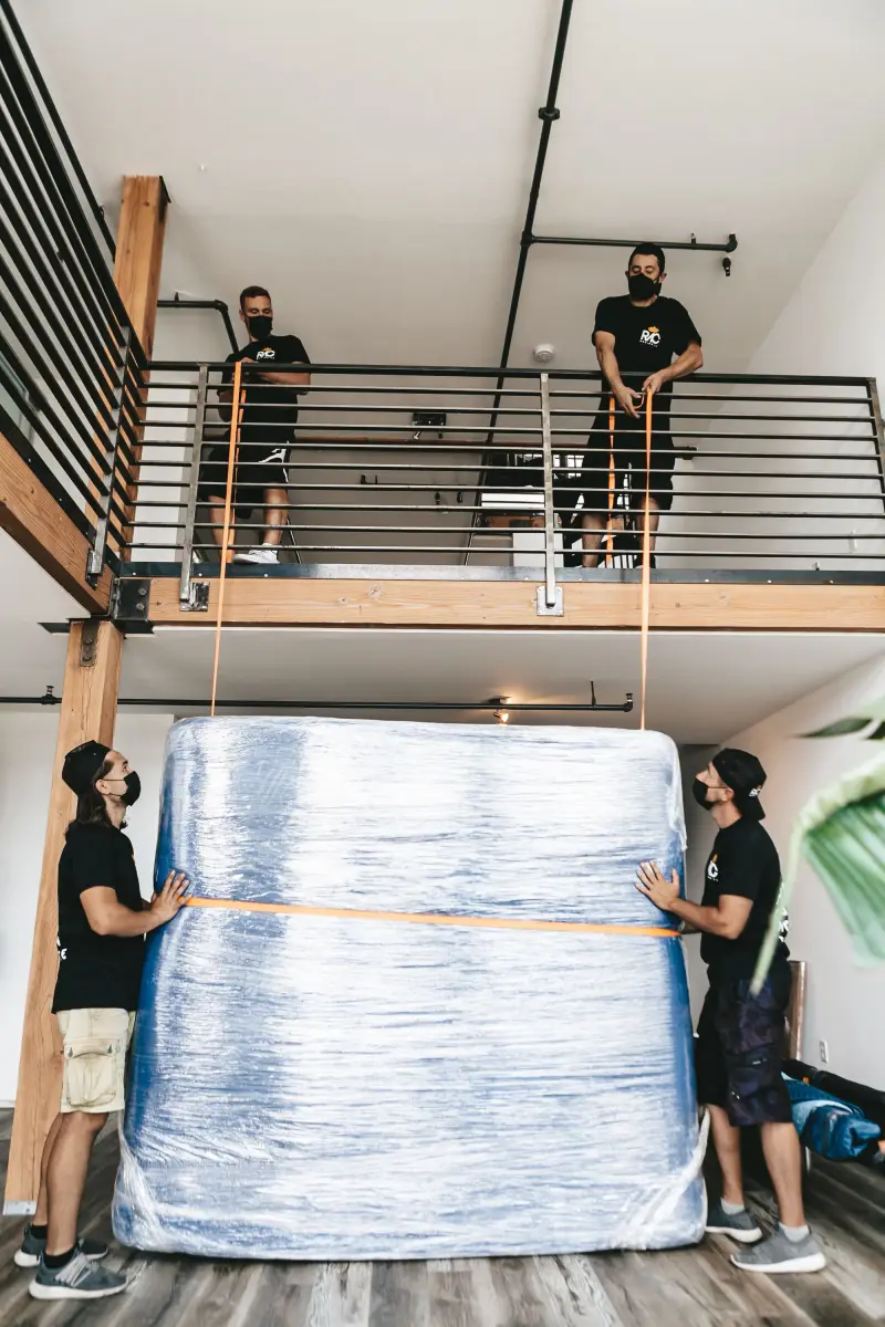 Movers lifting a large wrapped item with straps indoors